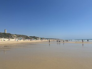 A beach with people, umbrellas, and a tower on a hill.