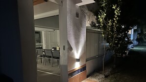 En bild av ett hus utifrån, med en kakelbeklädd entré, en dörr som leder in till en inomhusyta och ett litet träd.