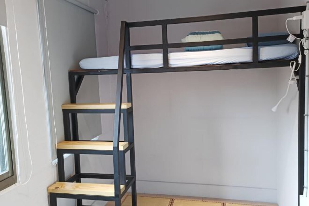 A bunk bed with a ladder, a window, and a power outlet on the wall.