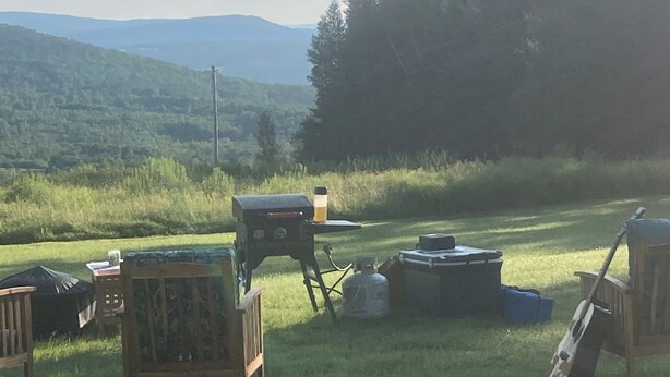 Un espace extérieur équipé d’un barbecue, d’une table avec une bouteille de gaz et d’un violon appuyé contre une chaise.