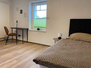 A bedroom with a bed, a desk, a chair, and a window with blinds.