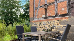 Un patio al aire libre con una mesa y sillas, rodeado de follaje y un muro de piedra.