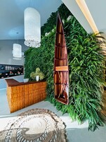 Un espace d’accueil doté d’un comptoir en bois, d’un grand mur végétal et de luminaires suspendus.