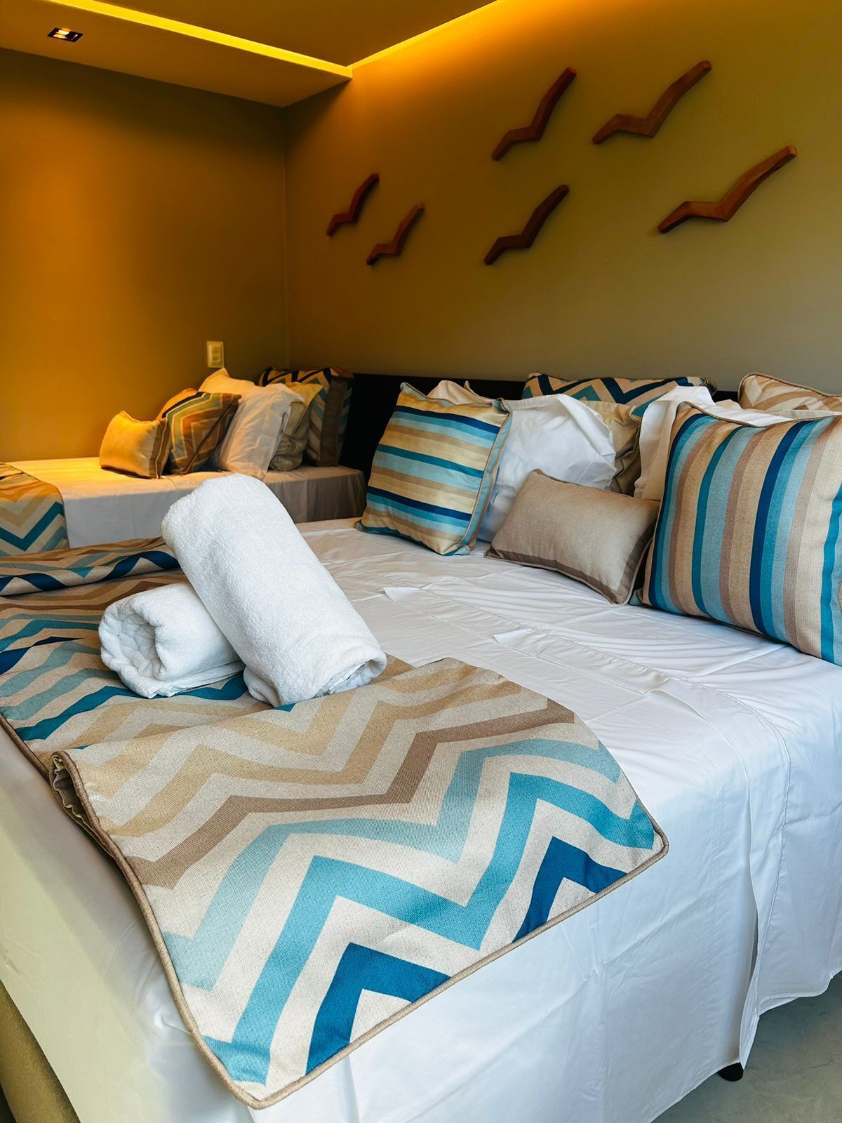 A hotel room with a large bed, multiple pillows, and a chevron-patterned throw.