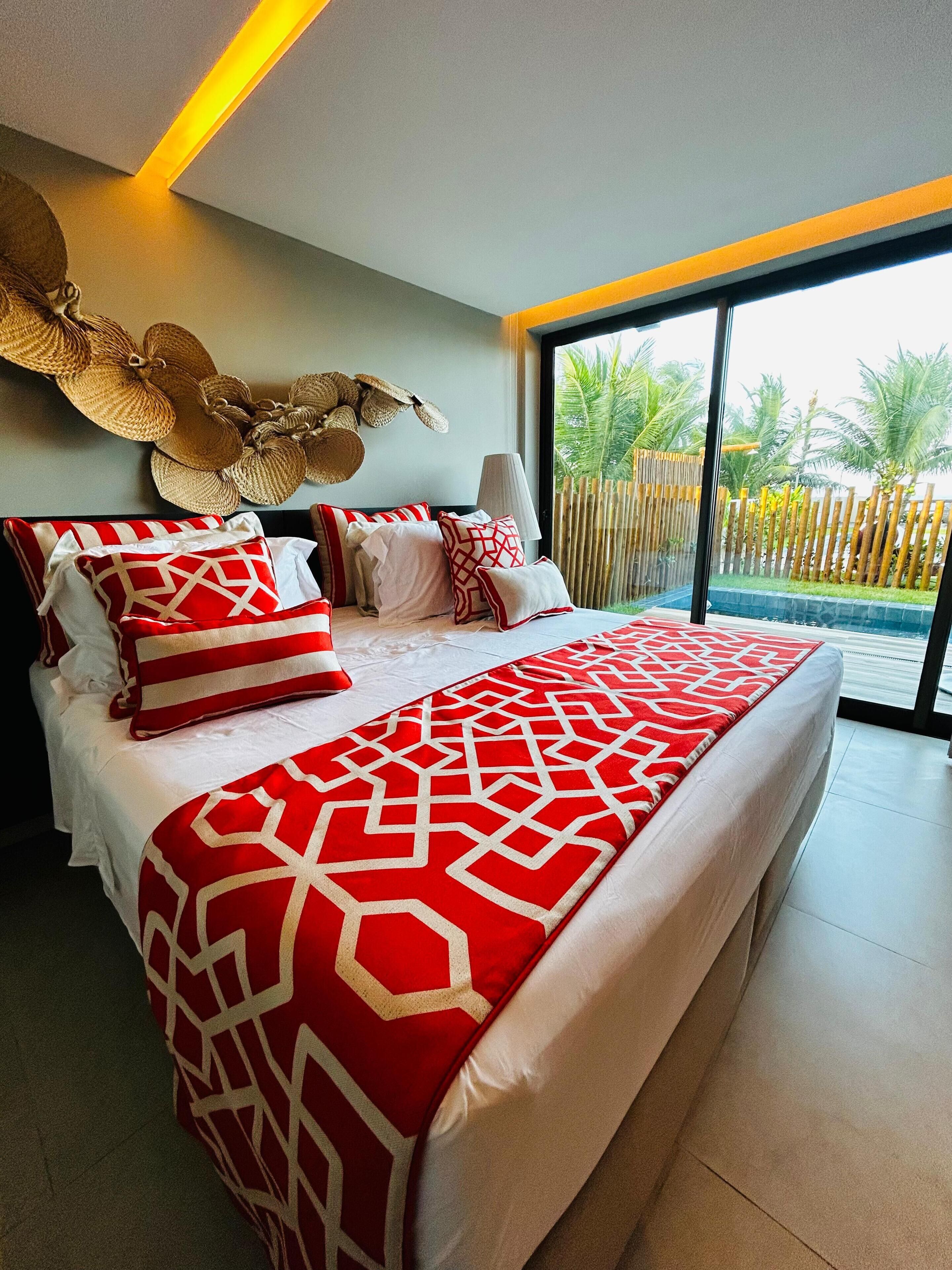 Un dormitorio moderno con una cama grande, un adorno en la pared y vistas a una piscina y palmeras.