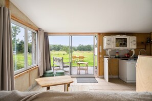 Une pièce dotée d’une porte-fenêtre coulissante donnant sur un espace extérieur, avec une table en bois, un banc et un coin cuisine équipé d’un meuble.
