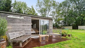 A wooden cabin with a bench, table, and glass door entrance. - Holiday Home 'Gîte Pour 4 Avec Sauna' with Shared Garden (Broons)