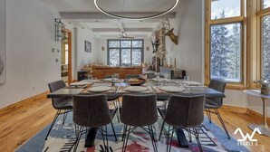 Ein Essbereich mit einem großen Tisch, gedeckt für sechs Personen, umgeben von Stühlen, mit einer modernen Pendelleuchte darüber.