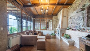 A spacious living room with a stone wall, wooden ceiling, and large windows. - Country House 'Casa Rural Magina' with Mountain View, Private Terrace and Wi-Fi (Fornelos de Montes)