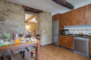 A kitchen with stone walls, wooden cabinets, a stainless steel refrigerator, a microwave, and a dishwasher.
