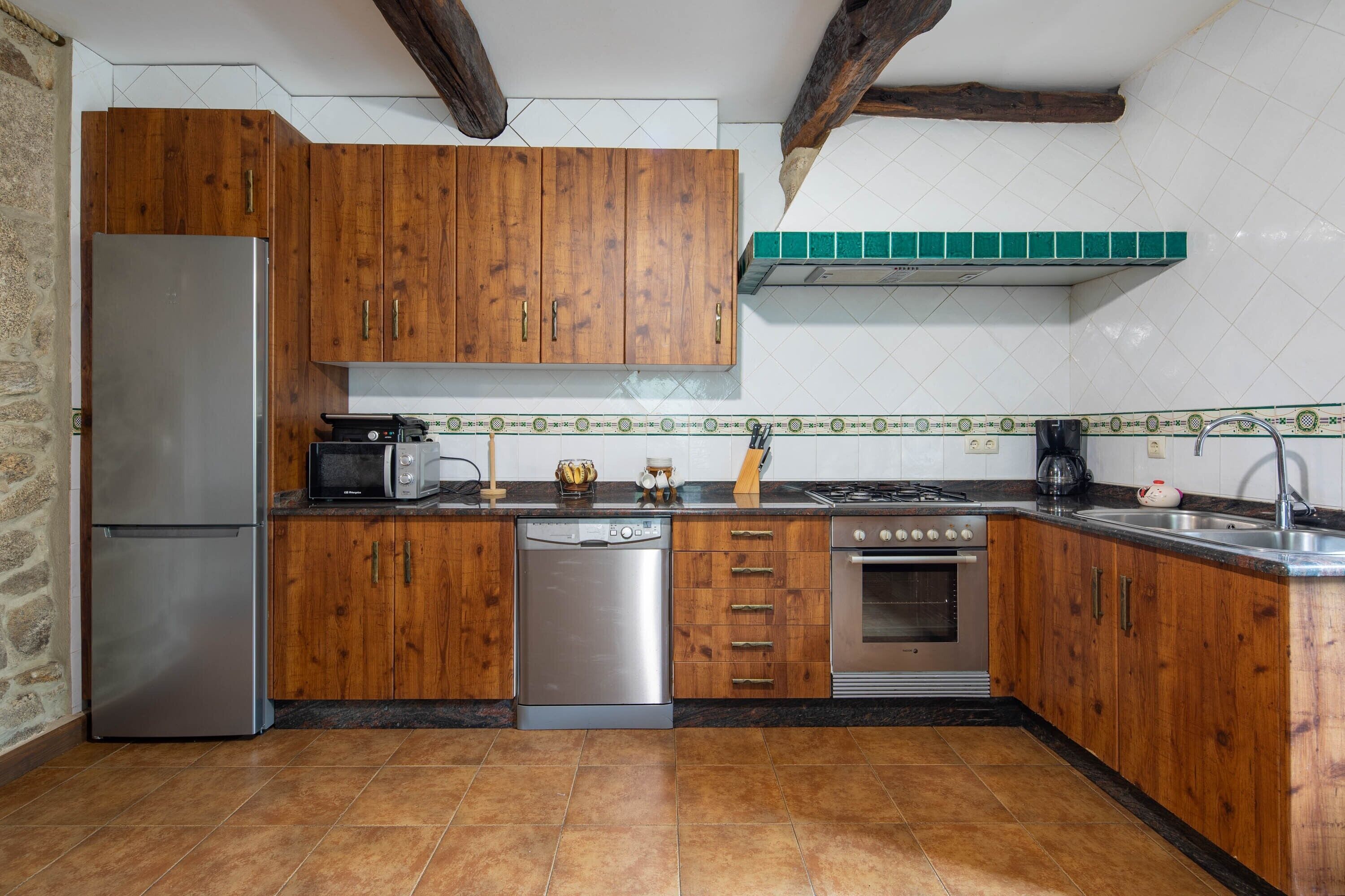 Una cucina con mobili in legno, un frigorifero in acciaio inossidabile, una lavastoviglie, un piano cottura e un lavello.