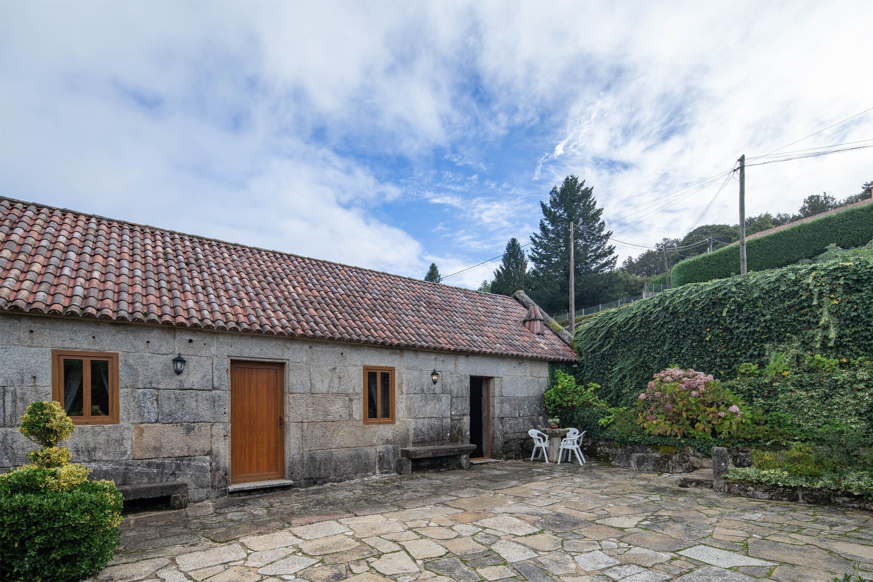 Una casa de piedra con techo de tejas, puerta de madera y patio de piedra con mobiliario exterior.