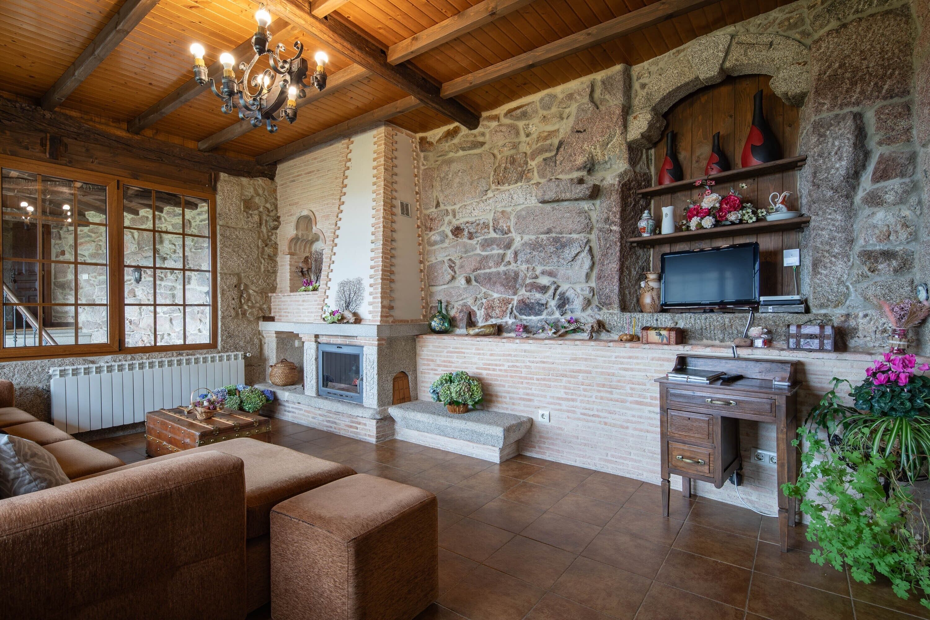 A cozy living room with a stone fireplace, wooden beams, a television, and a sofa.