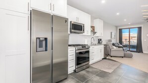 A modern kitchen with stainless steel appliances, a microwave, and a gas stove. There is a dining area with a sofa and a coffee table. The room has a large window providing a view of the outside. - Modern studio with huge balcony overlooking main street in Grand Lake (Grand Lake)