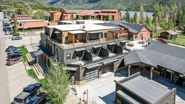 A modern hotel with a large parking lot, a covered outdoor seating area, and a view of mountains and a lake. - Modern studio with huge balcony overlooking main street in Grand Lake (Grand Lake)