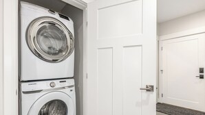 A laundry room with two stacked washing machines and a closed door. - Modern studio with huge balcony overlooking main street in Grand Lake (Grand Lake)