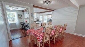 A dining area with a red and white checkered tablecloth, wooden chairs, and a kitchen in the background. - Lemonade Acres: Country Charm Made Convenient! (Ocala)