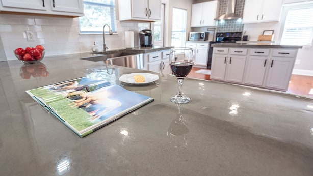 A kitchen with white cabinets, a stainless steel sink, and a glass island with a magazine, a glass of red wine, and a bowl of strawberries. - Lemonade Acres: Country Charm Made Convenient! (Ocala)