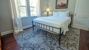 A bedroom with a bed, a nightstand, a lamp, and a window with curtains. - Lemonade Acres: Country Charm Made Convenient! (Ocala)