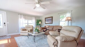 A living room with a beige sofa, a coffee table, and a ceiling fan. - Lemonade Acres: Country Charm Made Convenient! (Ocala)