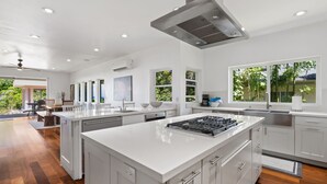 Una cocina amplia con una isla central, armarios blancos y ventanas grandes que ofrecen vistas a la vegetación.