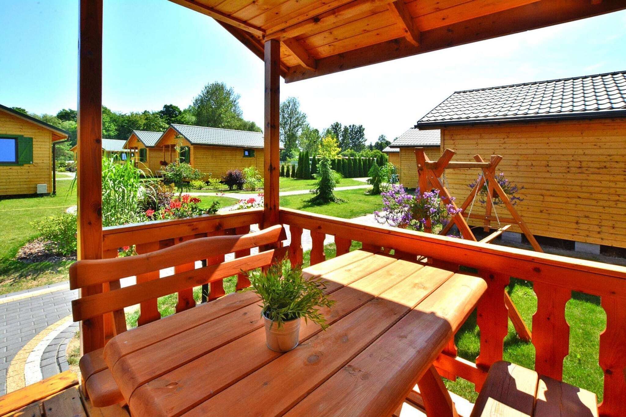 A wooden deck with benches and a table, overlooking a garden with small houses and a clear sky.