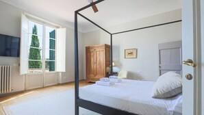 Un dormitorio con cama con dosel, un armario de madera, un radiador y una ventana con contraventanas.