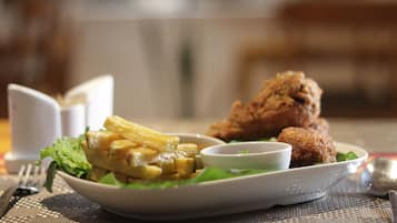 Un plato de comida con papas fritas, un producto empanizado y un recipiente pequeño con salsa, servido sobre una mesa con camino de mesa.