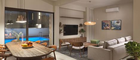 Un salon moderne avec un coin repas, une vue sur la piscine et un téléviseur à écran plat.