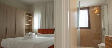 A bedroom with a bed, a bathroom with a shower, and a wooden wardrobe.