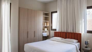 A bedroom with a bed, wooden wardrobe, shelves with toiletries, and a window with curtains.