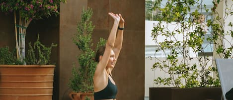 A person performing yoga by a poolside with potted plants and a bench nearby.