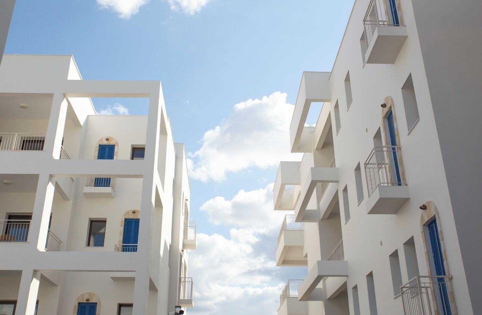 Ein modernes, mehrstöckiges Gebäude mit Balkonen und Fenstern, vor blauem Himmel mit Wolken.