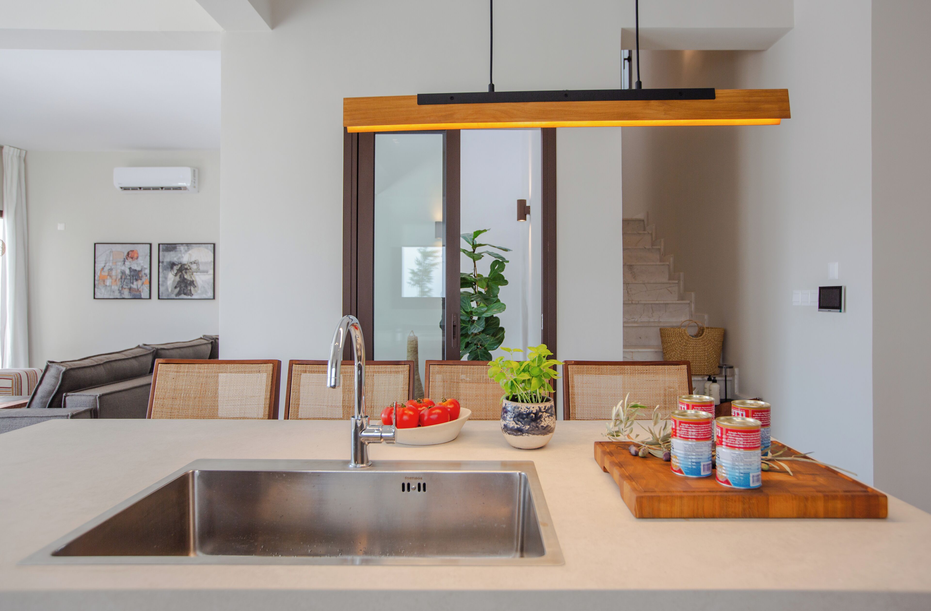 A modern kitchen with a stainless steel sink, a wooden cutting board with canned goods, and a potted plant.
