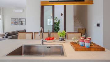 A modern kitchen with a stainless steel sink, a wooden cutting board with canned goods, and a potted plant.