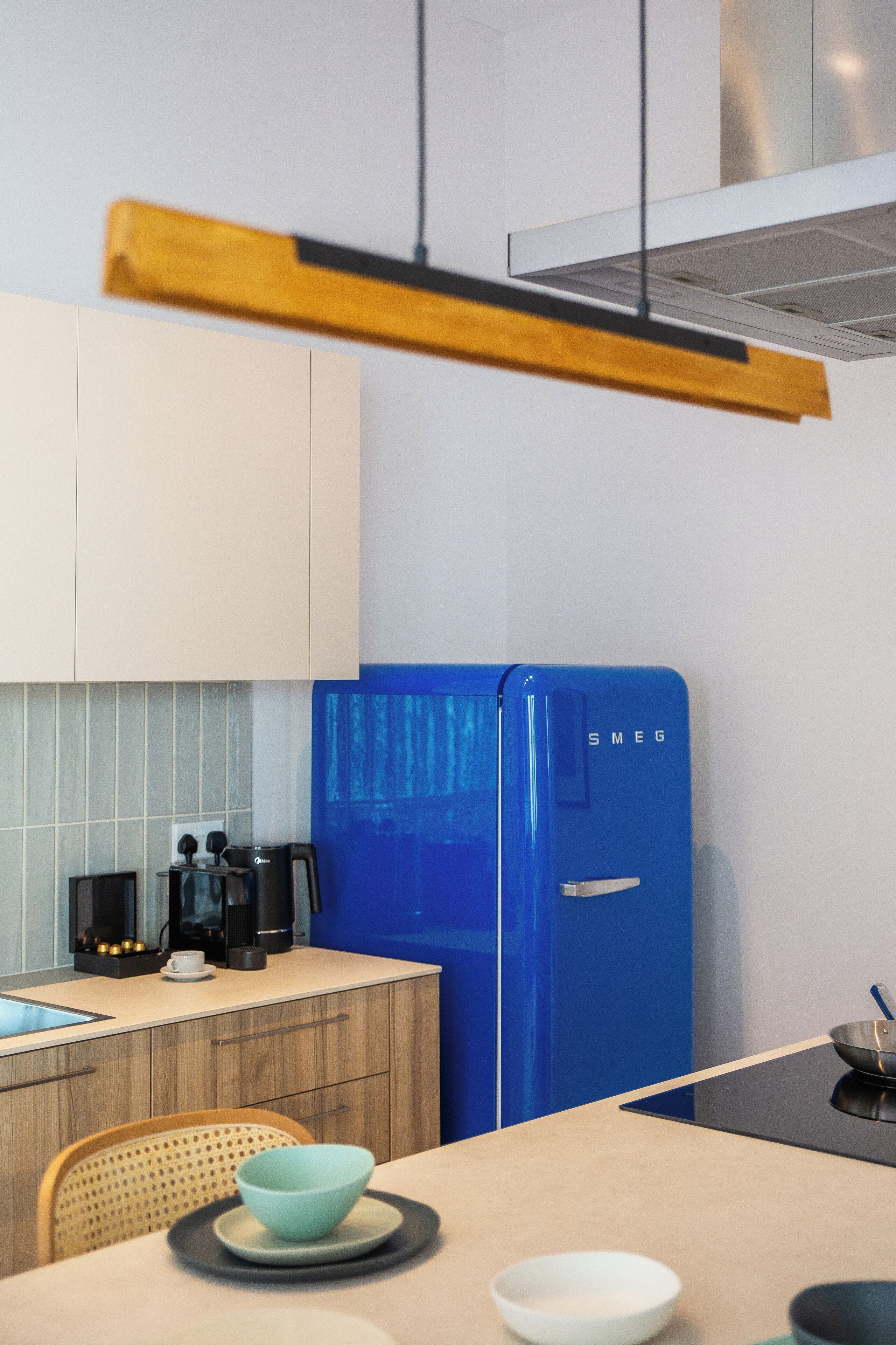 Une cuisine moderne avec un réfrigérateur bleu, des armoires en bois et un plan de travail de couleur claire.