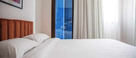 A hotel room with a bed, a headboard, a door with blue shutters, and a framed picture on the wall.