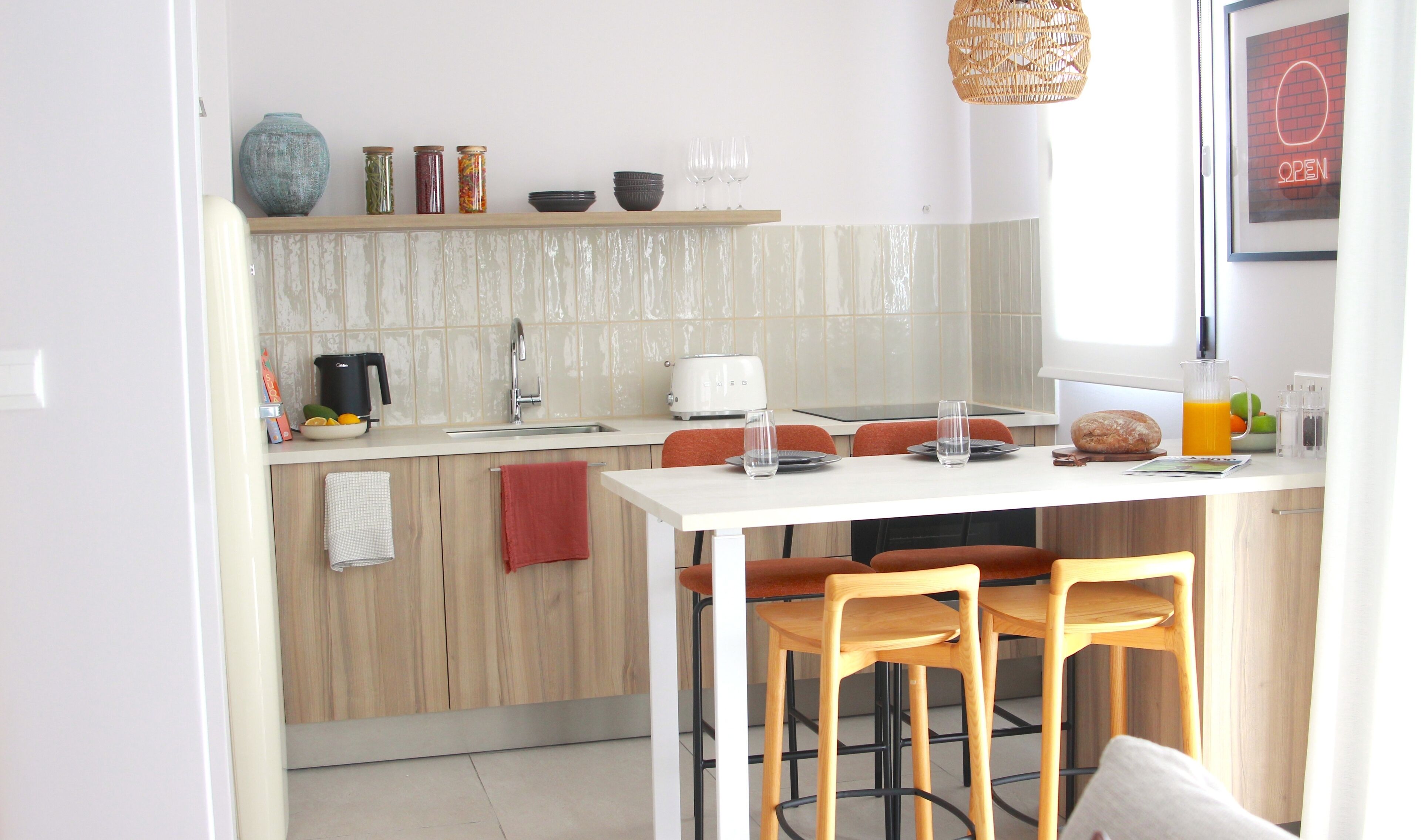 Une cuisine moderne avec un plan de travail blanc, des armoires en bois et un coin repas comprenant deux chaises en bois.