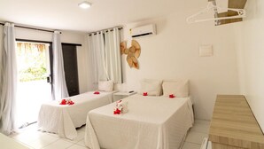A hotel room with two beds, a wooden desk, a small refrigerator, and a window with curtains. - Pousada Beach Garden (Ipojuca)