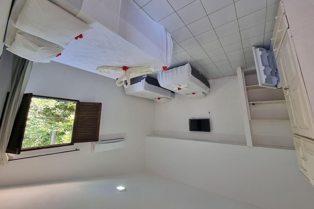 Habitación de hotel con dos camas, una ventana con persianas, unidad de aire acondicionado, televisor de pantalla plana y un mueble pequeño.