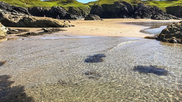 A beach with clear shallow waters, rocky terrain, and green hills in the background. - 4 bedroom accommodation in Tudweiliog (Tudweiliog)