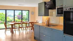 A modern kitchen with a dining area, large windows, and a view of greenery. - 4 bedroom accommodation in Tudweiliog (Tudweiliog)