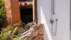 A stone wall with a metal showerhead attached to a white wall, a rustic chimney, and a tiled roof structure. - Casa Sole by Wonderful Italy (Olbia)