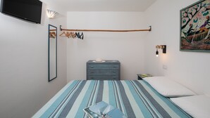 A bedroom with a bed, a dresser, a mirror, a TV, and a painting on the wall. - Casa Sole by Wonderful Italy (Olbia)