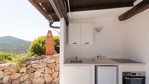 A compact kitchen with a stone wall, a sink, a small refrigerator, and an oven. - Casa Sole by Wonderful Italy (Olbia)
