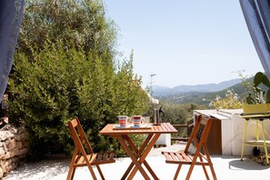 An outdoor patio with a wooden table and chairs, a stone wall, and a view of the countryside.