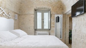 A bedroom with a large bed, a window with a view, and a flat-screen TV mounted on the wall.