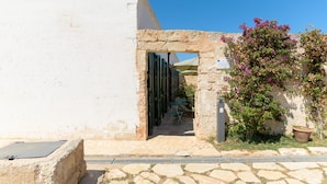 A stone archway leading to a covered outdoor seating area with a table and chairs.