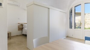 A room with a large sliding door, a bed with a wooden headboard, a small table, and a view of the outdoors through a large window.