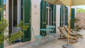 Un bâtiment avec des volets verts, une enseigne portant le chiffre « 2 », et des places assises à l’extérieur, avec une table et des chaises.